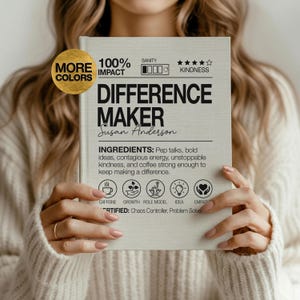 May include: A light-colored book titled "DIFFERENCE MAKER" by Susan Anderson. The cover includes the words "100% IMPACT", "SANITY", and "KINDNESS". The book's ingredients are listed as pep talks, bold ideas, contagious energy, unstoppable kindness, and coffee.