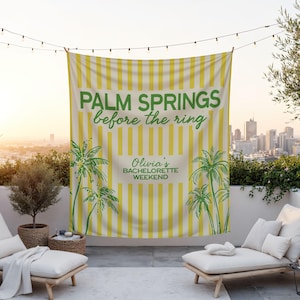 May include: A banner with yellow and white stripes and green text that reads "PALM SPRINGS before the ring" and "Olivia's BACHELORETTE WEEKEND". The banner also features green palm tree illustrations. The banner is hanging outdoors.