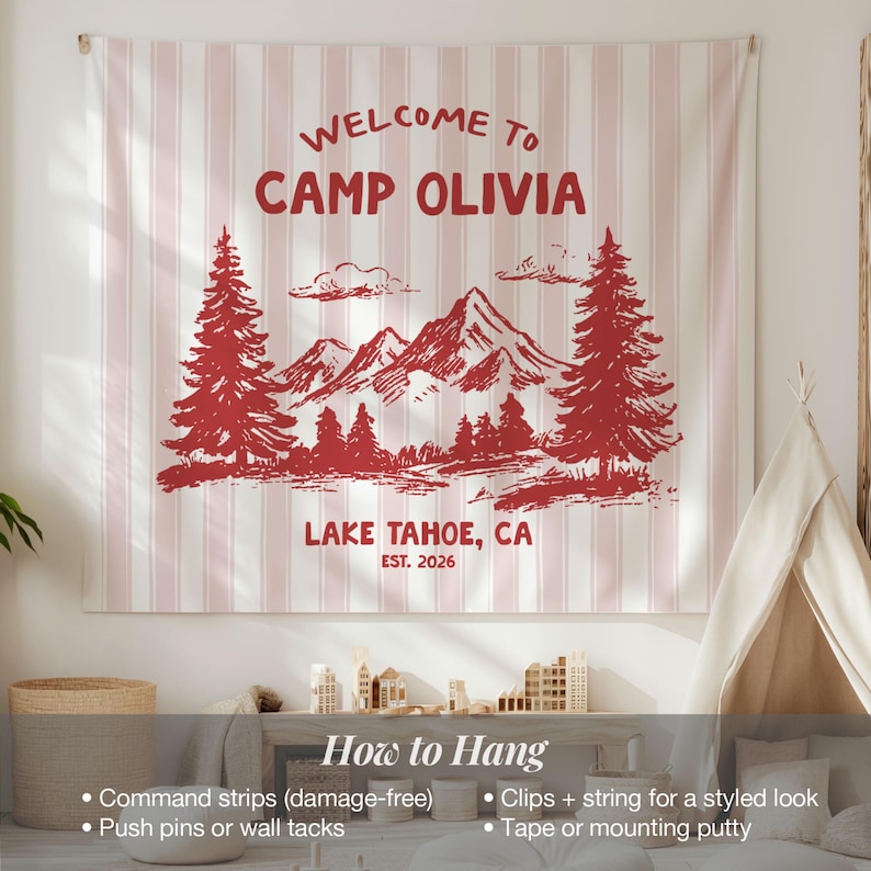 May include: A wall tapestry with a red and white striped background. The tapestry features a red illustration of mountains, trees, and the text "WELCOME TO CAMP OLIVIA LAKE TAHOE, CA EST. 2026". Instructions on how to hang the tapestry are also included.