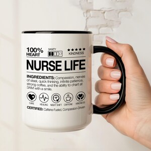 May include: White ceramic mug with a black handle and rim, featuring the text "NURSE LIFE" and a list of ingredients including "compassion" and "strong coffee." The mug also has icons and the words "CARE", "HEALING", "NIGHT SHIFT", "CAFFEINE", and "KINDNESS".