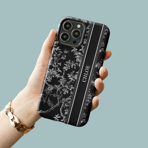 May include: Black phone case with a white floral pattern and a black stripe down the side that says "CHLOE".