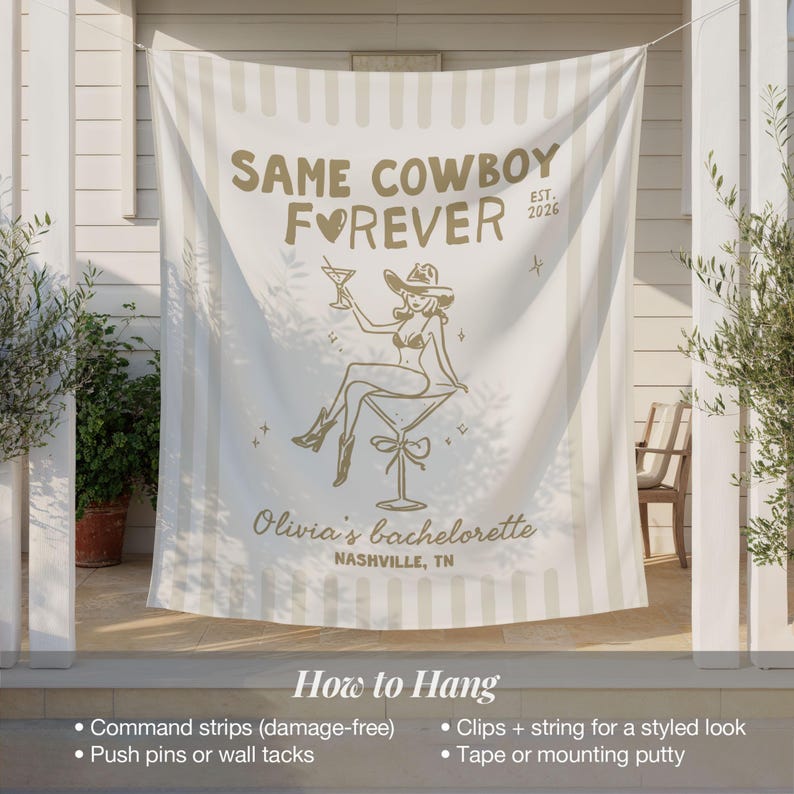 以下が含まれることがあります： 「SAME COWBOY FOREVER EST. 2026」と「Olivia's bachelorette NASHVILLE, TN」の文字が入った、白とベージュのストライプのバナー。カウボーイハットをかぶりカクテルを持つ女性の金のイラストが描かれています。バナーは屋外に吊るされています。