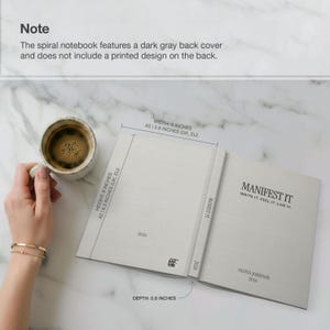 May include: Open spiral notebook with the text "MANIFEST IT" and the words "WRITE IT. FEEL IT. LIVE IT." The notebook is 6 inches wide, 8 inches high, and 0.6 inches deep. A cup of coffee sits next to the notebook.