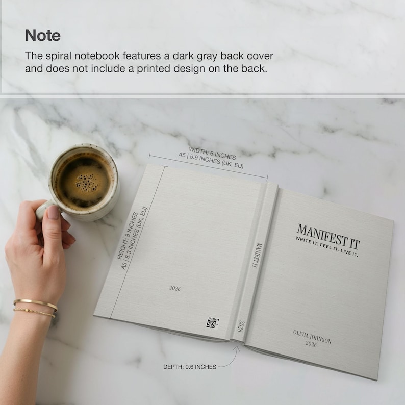 May include: Open spiral notebook with the text "MANIFEST IT" and the words "WRITE IT. FEEL IT. LIVE IT." The notebook is 6 inches wide, 8 inches high, and 0.6 inches deep. A cup of coffee sits next to the notebook.
