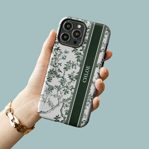 May include: A white phone case with a green floral pattern and a green stripe down the side. The stripe has the name "CHLOE" written on it.