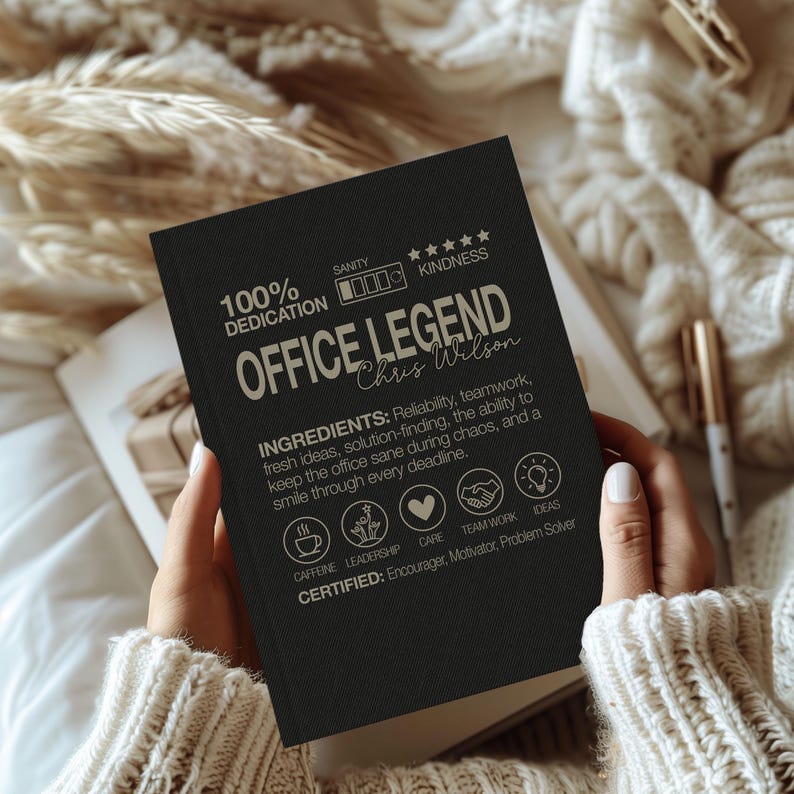 May include: A black notebook with the text "OFFICE LEGEND" and the name "Chris Wilson" in a handwritten font. The notebook also includes the words "100% DEDICATION" and "KINDNESS". The notebook is held open.