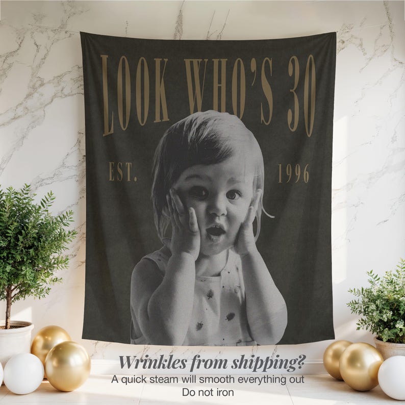 May include: A dark gray rectangular fabric wall hanging featuring a black and white photograph of a child with hands on their cheeks. The text "LOOK WHO'S 30" appears in large gold letters at the top, with "EST. 1996" printed in gold below the text.