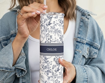 May include: A white and navy blue floral-patterned tumbler with a straw. The tumbler has a dark blue band with the name "CHLOE" in white lettering. The design features a detailed botanical print. The tumbler is cylindrical and appears to be insulated.