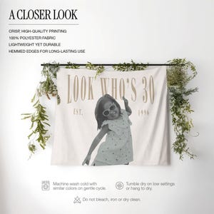 May include: A rectangular polyester wall tapestry featuring a black and white photograph of a child wearing sunglasses. The text reads LOOK WHO'S 30 and EST. 1996 in a tan serif font. The fabric is off-white with hemmed edges and is displayed hanging.