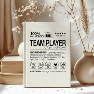May include: A wooden plaque with the words "TEAM PLAYER" and the name "Chris Wilson" in black. The plaque includes text about collaboration, kindness, and ingredients for teamwork, along with icons representing caffeine, support, teamwork, care, and growth.
