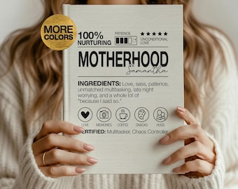 May include: A light-coloured book titled "Motherhood" with the name "Samantha" below the title. The book's cover includes text about ingredients like love, sass, and patience. A gold circle with the words "More Colors" is in the upper left corner.