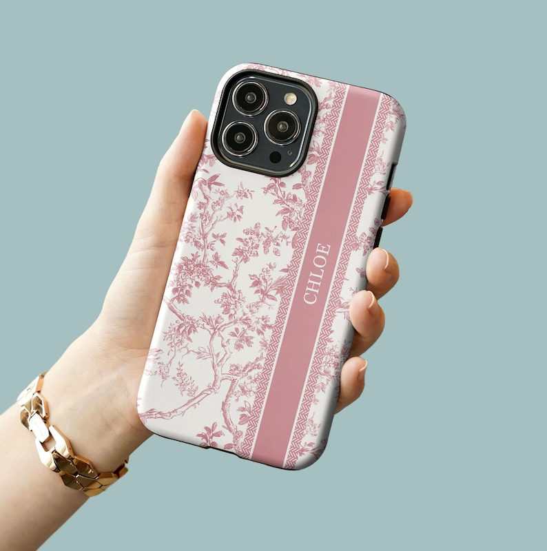 May include: A pink and white floral phone case with a pink stripe down the side. The stripe has the name "CHLOE" written on it.