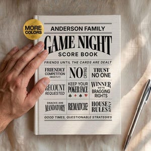 Puede incluir: Un libro de puntuación blanco titulado Anderson Family Game Night Score Book con texto negro y símbolos de cartas. La portada presenta frases como Friends Until The Cards Are Dealt, No Crying, Trust No One y Good Times, Questionable Strategies.