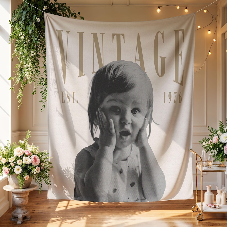 May include: A rectangular fabric wall tapestry featuring a large black and white photograph of a child with hands on their cheeks. The word VINTAGE is printed in large beige letters at the top, with EST. 1976 printed in smaller beige text below.