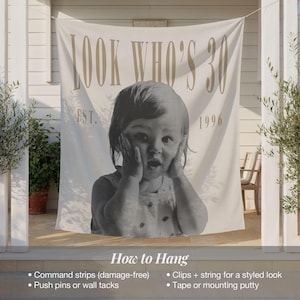 May include: A large off-white fabric banner featuring the text "LOOK WHO'S 30" at the top and "EST. 1996" below. The center displays a black and white photograph of a young child with hands pressed against their cheeks in a surprised expression.
