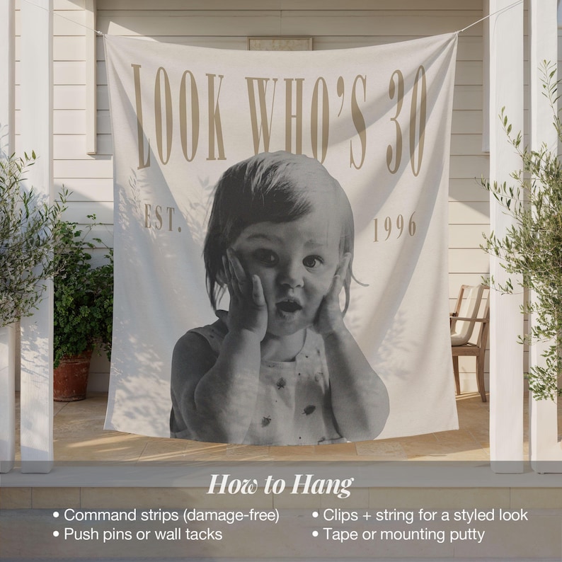May include: A large off-white fabric banner featuring the text "LOOK WHO'S 30" at the top and "EST. 1996" below. The center displays a black and white photograph of a young child with hands pressed against their cheeks in a surprised expression.