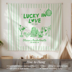Pode incluir: Uma tape&ccedil;aria de parede branca com listras verticais verde claro. Apresenta texto e ilustra&ccedil;&otilde;es verdes, incluindo "LUCKY IN LOVE", um martini, dados, uma m&aacute;quina ca&ccedil;a-n&iacute;queis, cartas de baralho e uma bola de discoteca. O texto na parte inferior diz "Olivia's bachelorette, Las Vegas, NV."