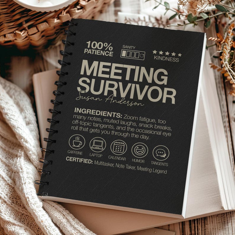 May include: A black spiral-bound notebook with the text "MEETING SURVIVOR" and the name "Susan Anderson". The notebook includes icons for caffeine, laptop, calendar, humor, and tangents. The text also lists ingredients for surviving meetings.