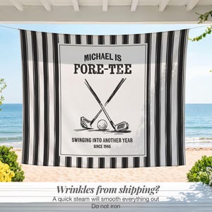 May include: A black and white striped beach towel with a central white panel featuring golf clubs, a ball, and the text "MICHAEL IS FORE-TEE". The towel also includes the text "SWINGING INTO ANOTHER YEAR SINCE 1986".