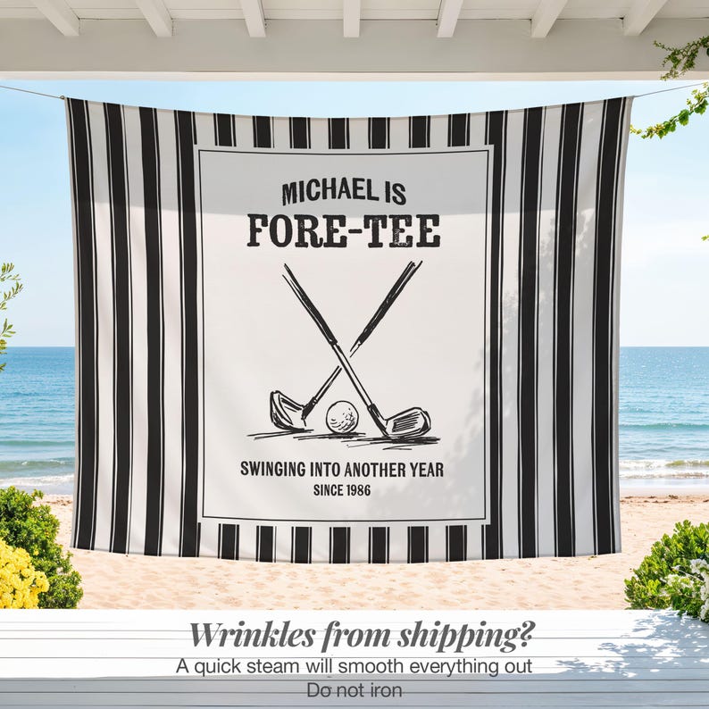 May include: A black and white striped beach towel with a central white panel featuring golf clubs, a ball, and the text "MICHAEL IS FORE-TEE". The towel also includes the text "SWINGING INTO ANOTHER YEAR SINCE 1986".