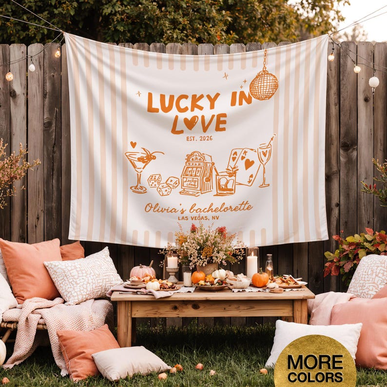 Pode incluir: Uma cena de festa ao ar livre com uma faixa que diz "LUCKY IN LOVE" e "Olivia's bachelorette LAS VEGAS, NV". A faixa tem um fundo listrado e ilustra&ccedil;&otilde;es de coquet&eacute;is, dados e cartas de baralho. A cena inclui almofadas, ab&oacute;boras e uma mesa de madeira.