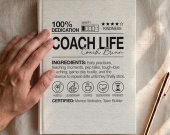 May include: A cream-colored hardcover notebook with black text reading COACH LIFE Coach Brian. The cover lists ingredients like early practices, teaching moments, pep talks, and patience, alongside icons for hustle, leadership, coffee, dedication, and patience.