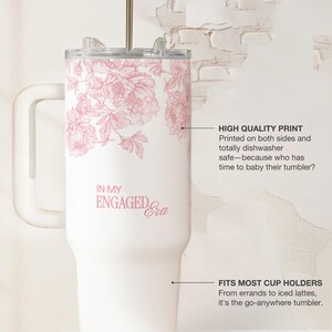 May include: White tumbler with a pink floral design and the text "IN MY ENGAGED Era." The tumbler has a handle, a lid, and a straw. The text "HIGH QUALITY PRINT" and "FITS MOST CUP HOLDERS" are also visible.
