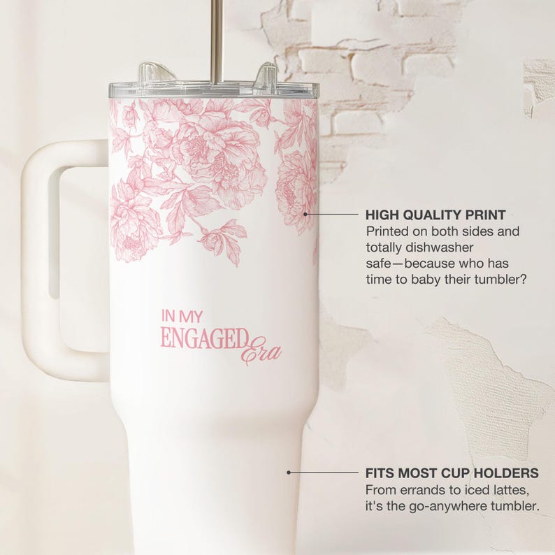 May include: White tumbler with a pink floral design and the text "IN MY ENGAGED Era." The tumbler has a handle, a lid, and a straw. The text "HIGH QUALITY PRINT" and "FITS MOST CUP HOLDERS" are also visible.