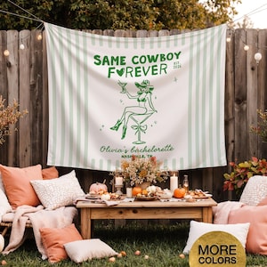 以下が含まれることがあります： 「SAME COWBOY FOREVER」の文字とカウボーイハットをかぶった女性のグラフィックが描かれた、白と緑のストライプのタペストリー。タペストリーは、クッション、カボチャ、木製のテーブルを備えた独身パーティーのセットアップの一部です。