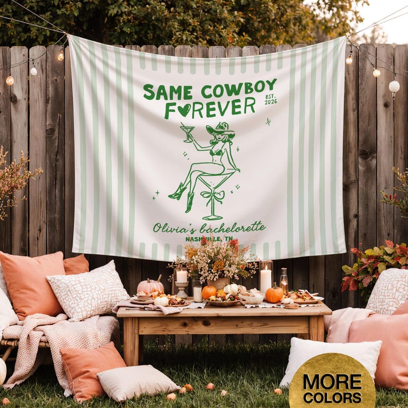 以下が含まれることがあります： 「SAME COWBOY FOREVER」の文字とカウボーイハットをかぶった女性のグラフィックが描かれた、白と緑のストライプのタペストリー。タペストリーは、クッション、カボチャ、木製のテーブルを備えた独身パーティーのセットアップの一部です。