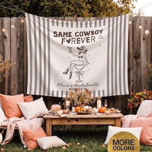 以下が含まれることがあります： 「SAME COWBOY FOREVER」の文字とカウボーイハットをかぶった女性のグラフィックが描かれた、白とグレーのストライプのバナー。「Olivia's bachelorette, Nashville, TN」と書かれています。枕、カボチャ、木製のテーブルが写っています。