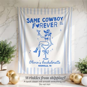 以下が含まれることがあります： 「SAME COWBOY FOREVER」の文字と、カウボーイハットをかぶった女性がカクテルを持っているイラストが描かれた、白と青のストライプのバチェロレッテパーティー用タペストリー。「Olivia's bachelorette, Nashville, TN」の文字も含まれています。
