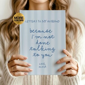 May include: A light blue and white vertically striped hardback book with the text "LETTERS TO MY HUSBAND because I'm not done talking to you LOVE, OLIVIA" printed in dark blue script and block lettering on the front cover.