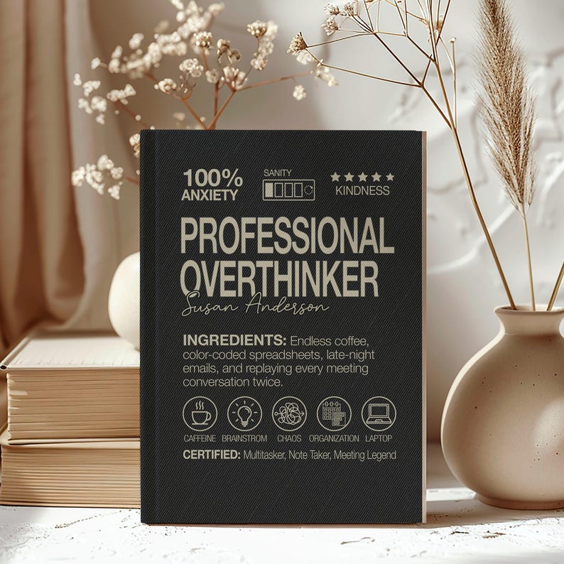 May include: A black notebook with the words "PROFESSIONAL OVERTHINKER" in white. The notebook lists ingredients like coffee and spreadsheets. The cover also states "100% Anxiety" and "Kindness".