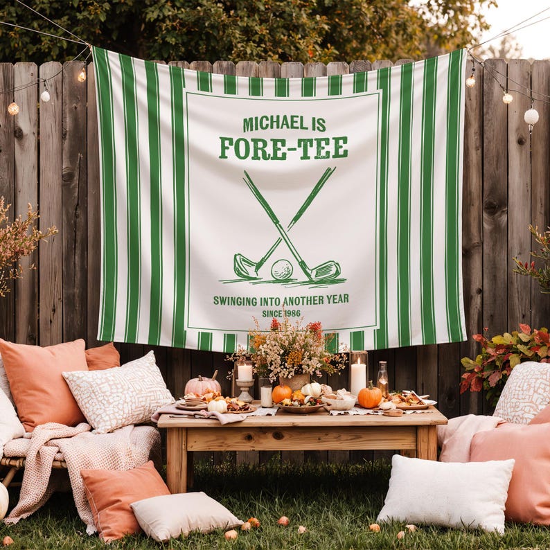 May include: A white and green striped banner with the text "MICHAEL IS FORE-TEE" and a golf-themed graphic. The banner is displayed outdoors, with a wooden table set for a gathering.