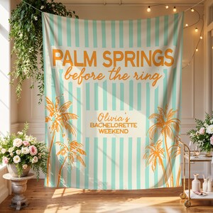 May include: A large, rectangular backdrop with vertical stripes in cream and light blue. The text "PALM SPRINGS before the ring" is in orange, along with palm tree illustrations. The text "Olivia's BACHELORETTE WEEKEND" is also present.