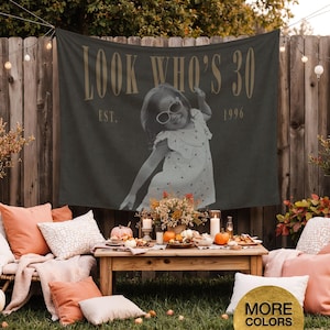 May include: A dark gray rectangular fabric banner featuring the text LOOK WHO'S 30 and EST. 1996 in a light tan font. The center of the banner displays a black and white photograph of a young child wearing sunglasses and a patterned dress.