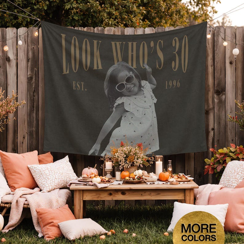 May include: A dark gray rectangular fabric banner featuring the text LOOK WHO'S 30 and EST. 1996 in a light tan font. The center of the banner displays a black and white photograph of a young child wearing sunglasses and a patterned dress.