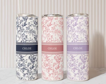 May include: Three personalized tumblers with floral patterns in navy, pink, and lavender. Each tumbler has a band with the name "CHLOE" and a clear lid. One tumbler has a straw. The text "MORE COLORS AVAILABLE" is at the bottom.