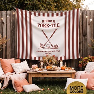 May include: A white and burgundy striped banner with the text "JESSICA IS FORE-TEE" and golf-themed graphics. The banner is displayed outdoors, with a wooden table set for a gathering, surrounded by pillows and pumpkins.
