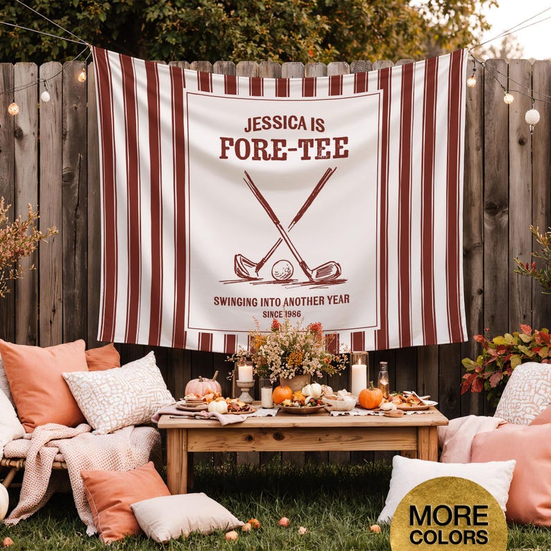May include: A white and burgundy striped banner with the text "JESSICA IS FORE-TEE" and golf-themed graphics. The banner is displayed outdoors, with a wooden table set for a gathering, surrounded by pillows and pumpkins.