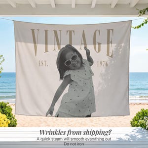 May include: A rectangular fabric wall hanging featuring a black and white photograph of a child wearing sunglasses and a patterned dress. The text VINTAGE is printed in large tan letters above the photo, with EST. 1976 printed in smaller tan text.