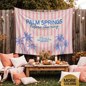 May include: A pink and cream striped backdrop with blue text that reads "Palm Springs before the ring" and "Olivia's Bachelorette Weekend". Palm tree illustrations are also featured. The scene includes a wooden table with food and pillows.