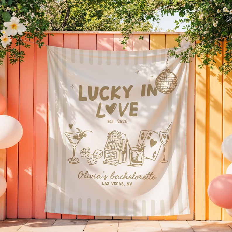 Pode incluir: Uma faixa de tecido creme com o texto "LUCKY IN LOVE" e "EST. 2026" em dourado. A faixa apresenta ilustra&ccedil;&otilde;es de um martini, dados, uma m&aacute;quina ca&ccedil;a-n&iacute;queis, cartas de baralho e uma bola de discoteca. O texto "Olivia's bachelorette LAS VEGAS, NV" tamb&eacute;m est&aacute; inclu&iacute;do.