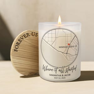 May include: A frosted glass candle with a lit wick, featuring a black circular map graphic of Newport Beach, CA, with a red heart, the text "Where it all started", "SAMANTHA & JACOB", and "JULY 12, 2025". A round bamboo lid with "FOREVER US" is beside it.