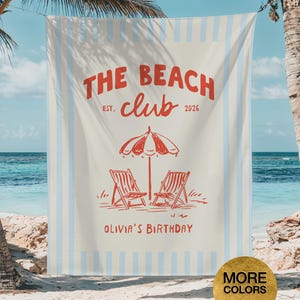 Może przedstawiać: Prostokątny ręcznik plażowy z kremowym tłem i pionowymi jasnoniebieskimi pasami. Na środku znajduje się czerwony napis THE BEACH CLUB EST. 2026, czerwona ilustracja parasola plażowego z dwoma krzesłami oraz napis OLIVIA'S BIRTHDAY.