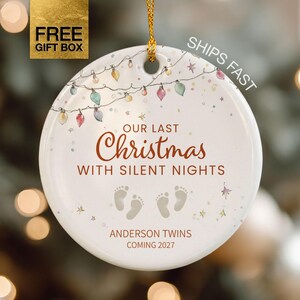 May include: A round white ceramic ornament featuring a string of colorful Christmas lights, the text "OUR LAST Christmas WITH SILENT NIGHTS," two pairs of baby footprints, and the text "ANDERSON TWINS COMING 2027" in brown lettering.