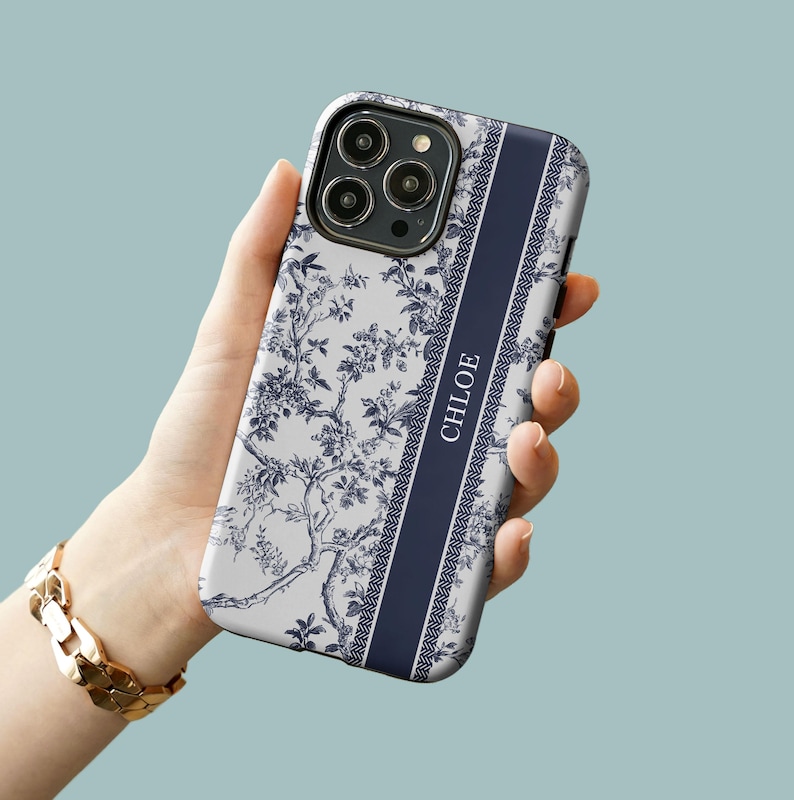 May include: A white phone case with a blue floral pattern and a navy blue stripe down the side. The stripe has the name "CHLOE" printed on it in white.