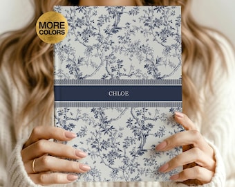 May include: A hardcover journal featuring a light gray background with a dark blue floral toile pattern. A horizontal dark blue band across the center displays the name CHLOE in white text, bordered by a thin herringbone pattern.