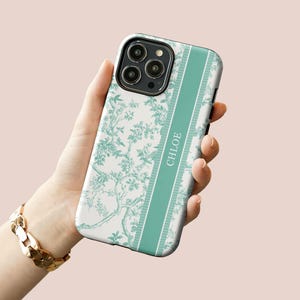 May include: A white phone case with a green floral pattern and a green stripe down the side. The stripe has the name "CHLOE" written on it.